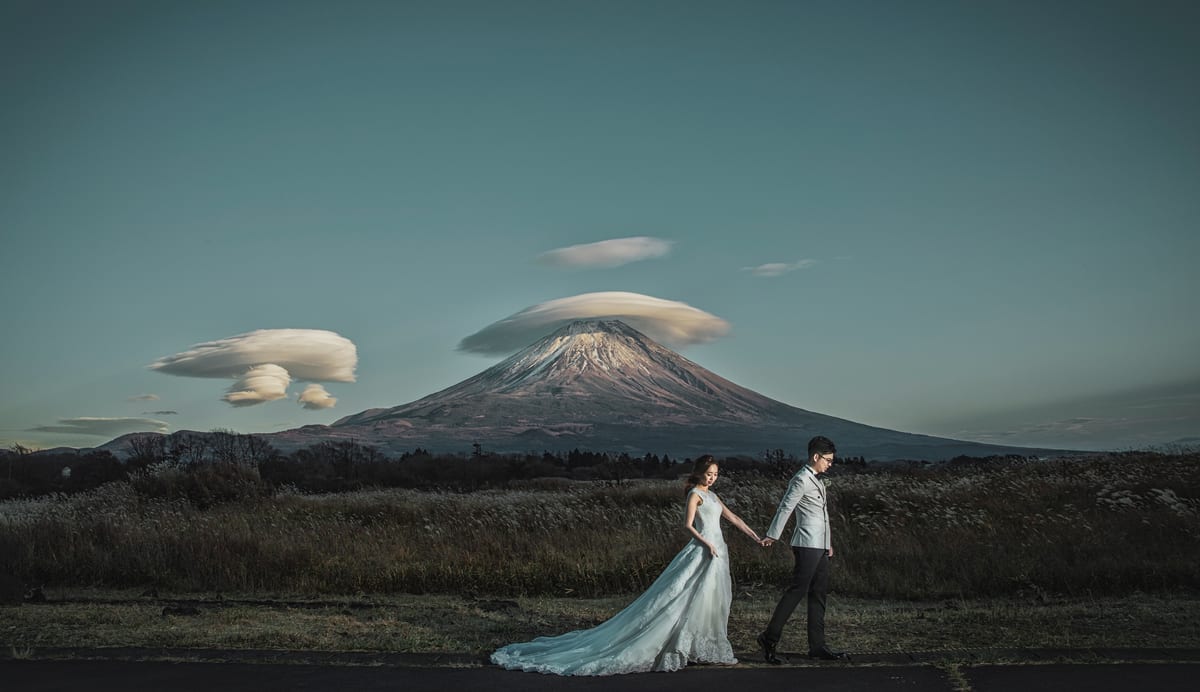 A bride and groom walking through a field with Mount Fuji behind them