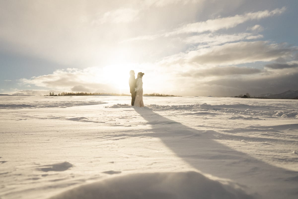 A bride and groom silhouetted by the sun in a snowy field