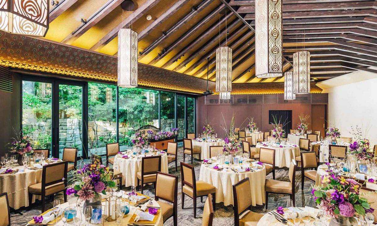 A garden-facing banquet room set with round tables and purple flowers