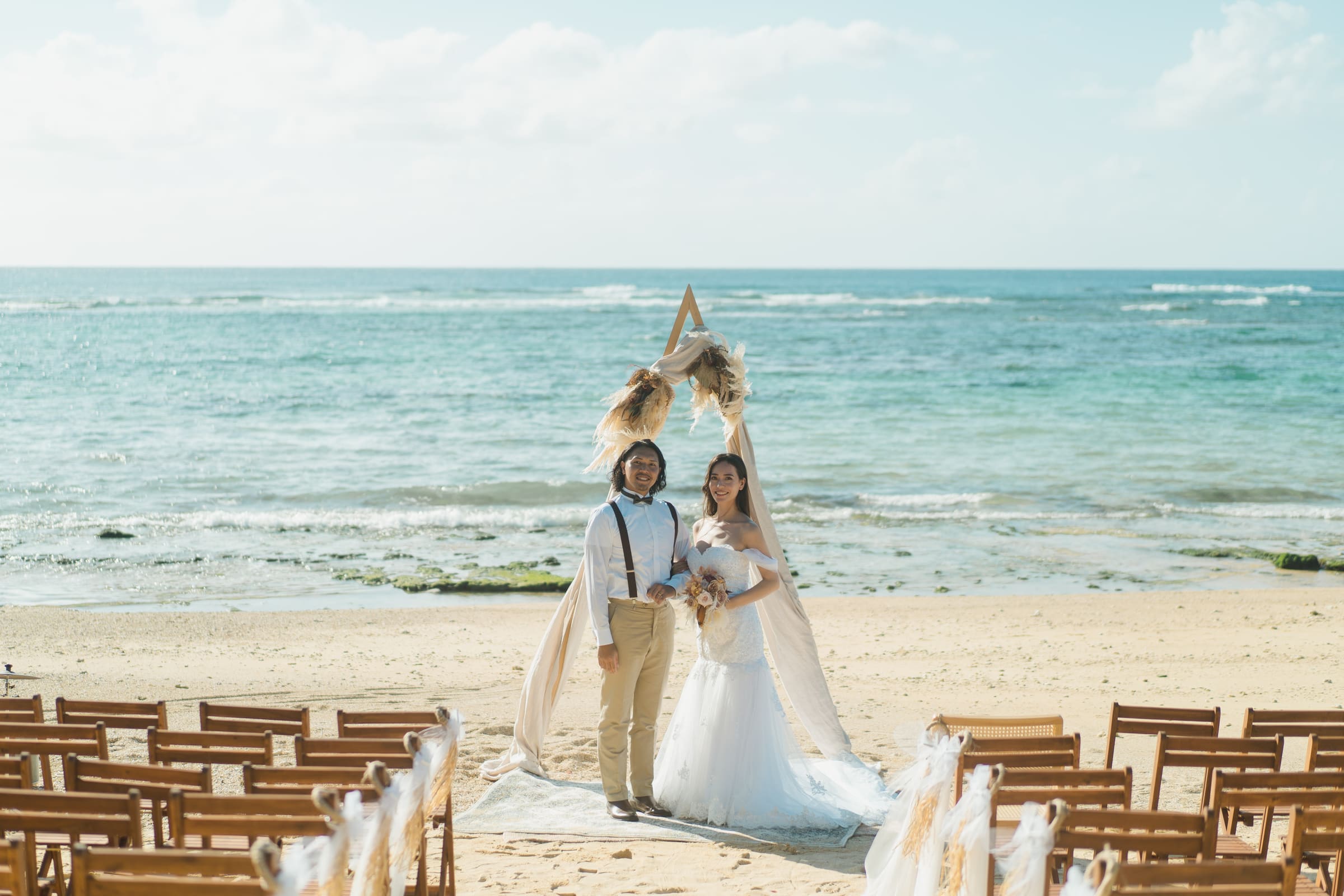 A newly married couple standing beneath an arch on the beach