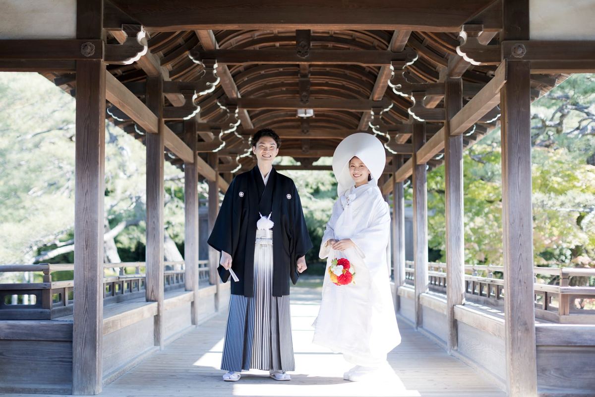 A couple in Japanese wedding attire beneath the Taiheikaku covered bridge