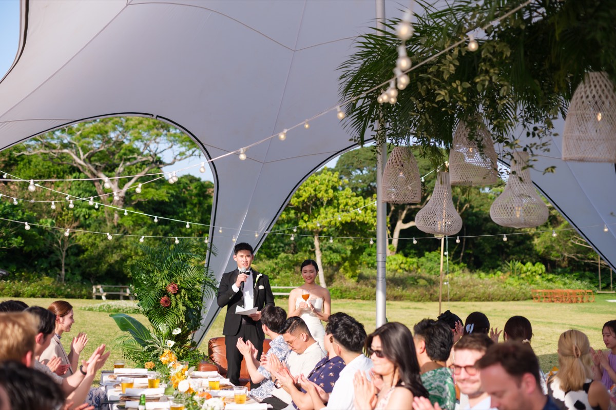 The couple speaking to guests during a garden reception beneath the canopy