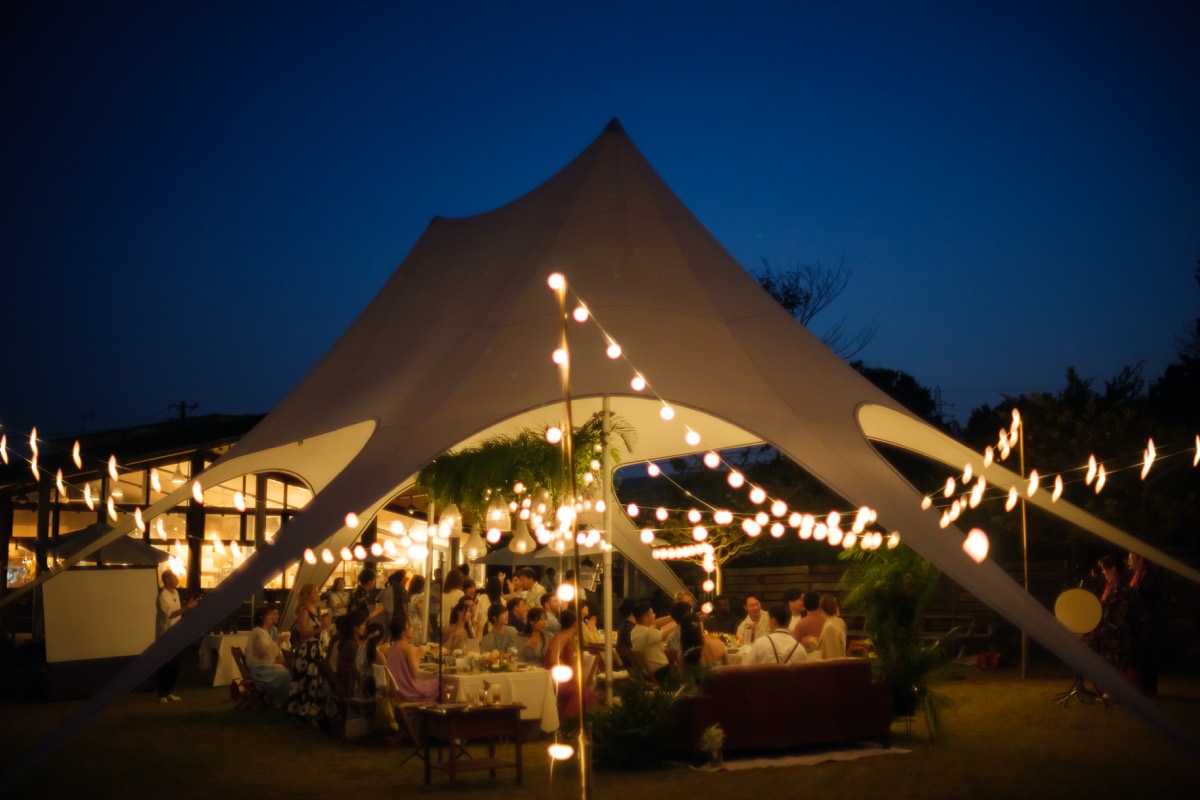 An illuminated canopy tent hosting a garden reception after dark