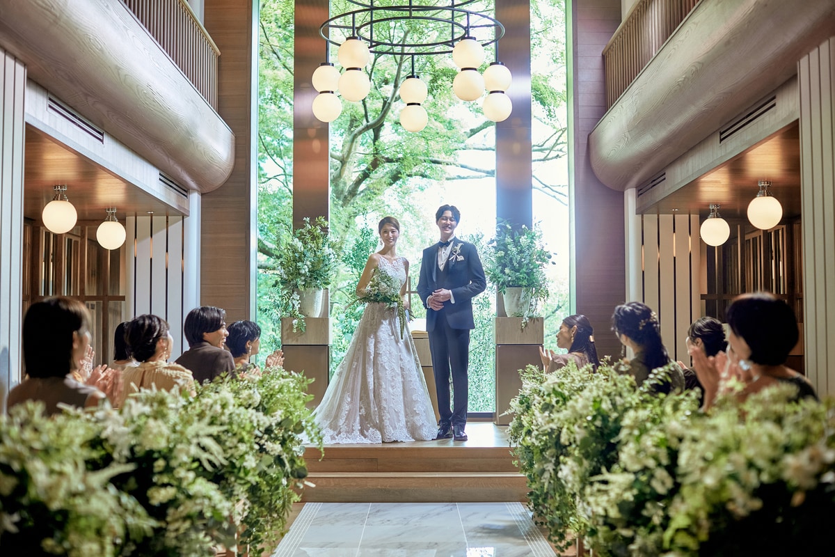 A wedding couple entering a wood-toned chapel lined with flowers and guests