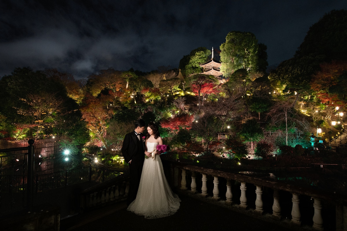 A wedding couple standing before the illuminated garden and pagoda at night