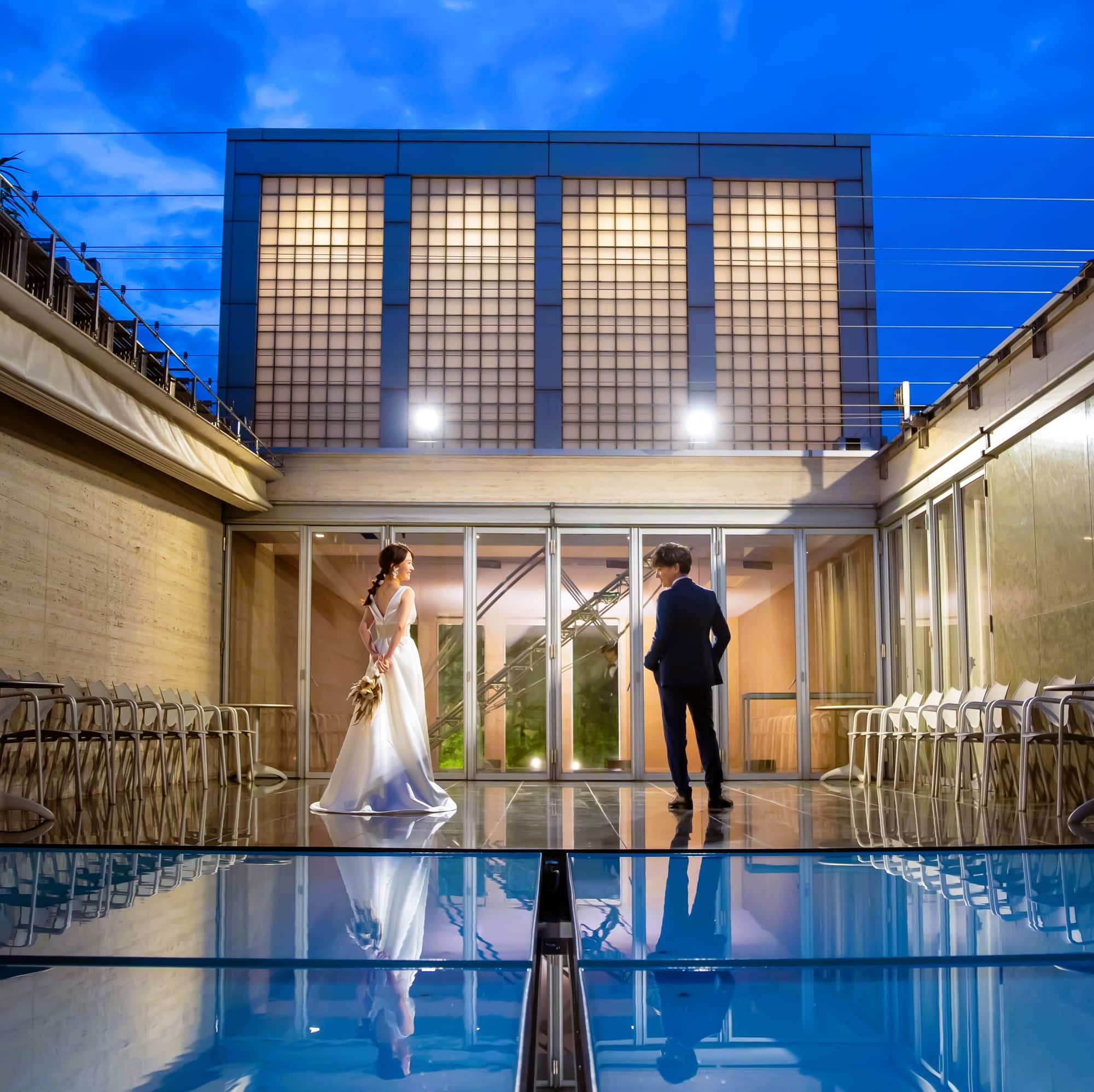 A bride and groom facing each other in the illuminated courtyard at dusk