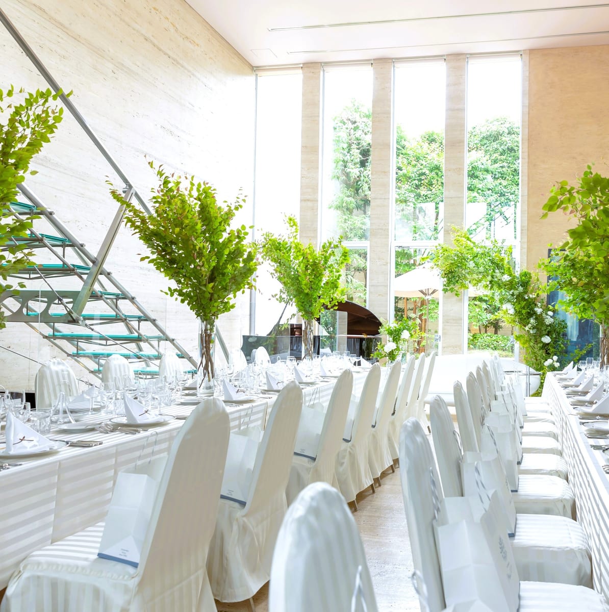 A bright reception room set with long dining tables and greenery