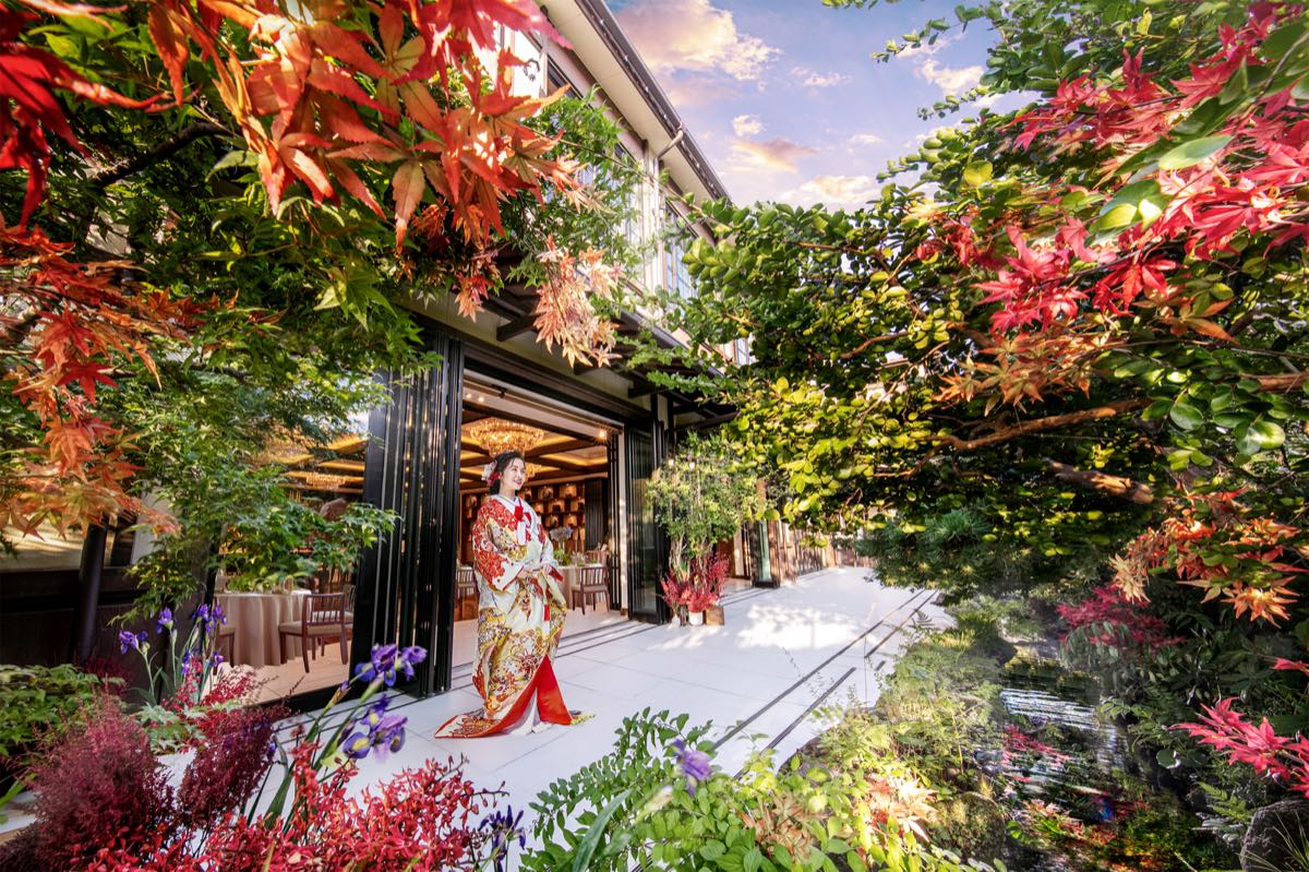 Bride in a colorful kimono standing beside an autumn garden