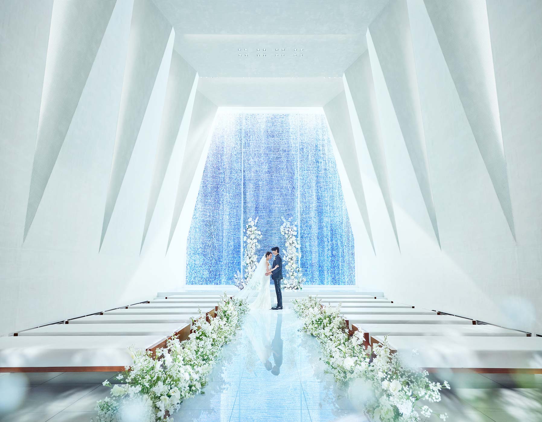 A couple standing at the altar of the white chapel with a blue waterfall backdrop