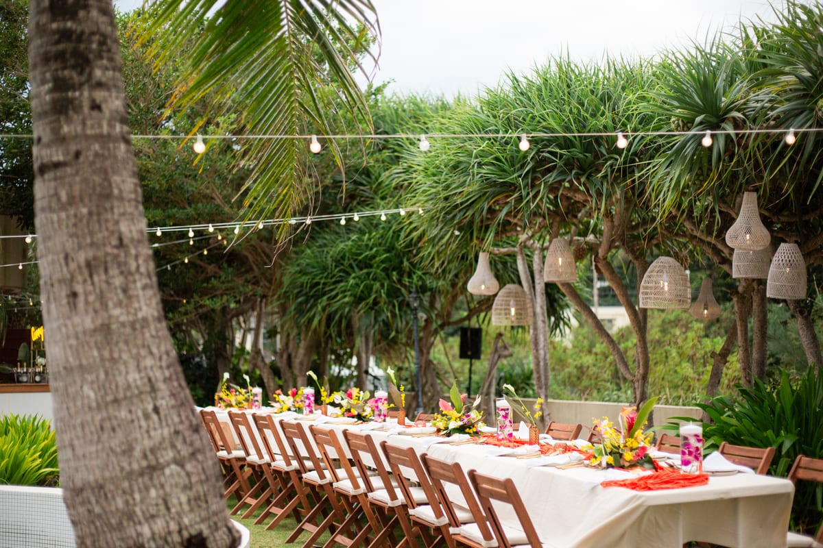 A long reception table set beneath lights in the tropical garden