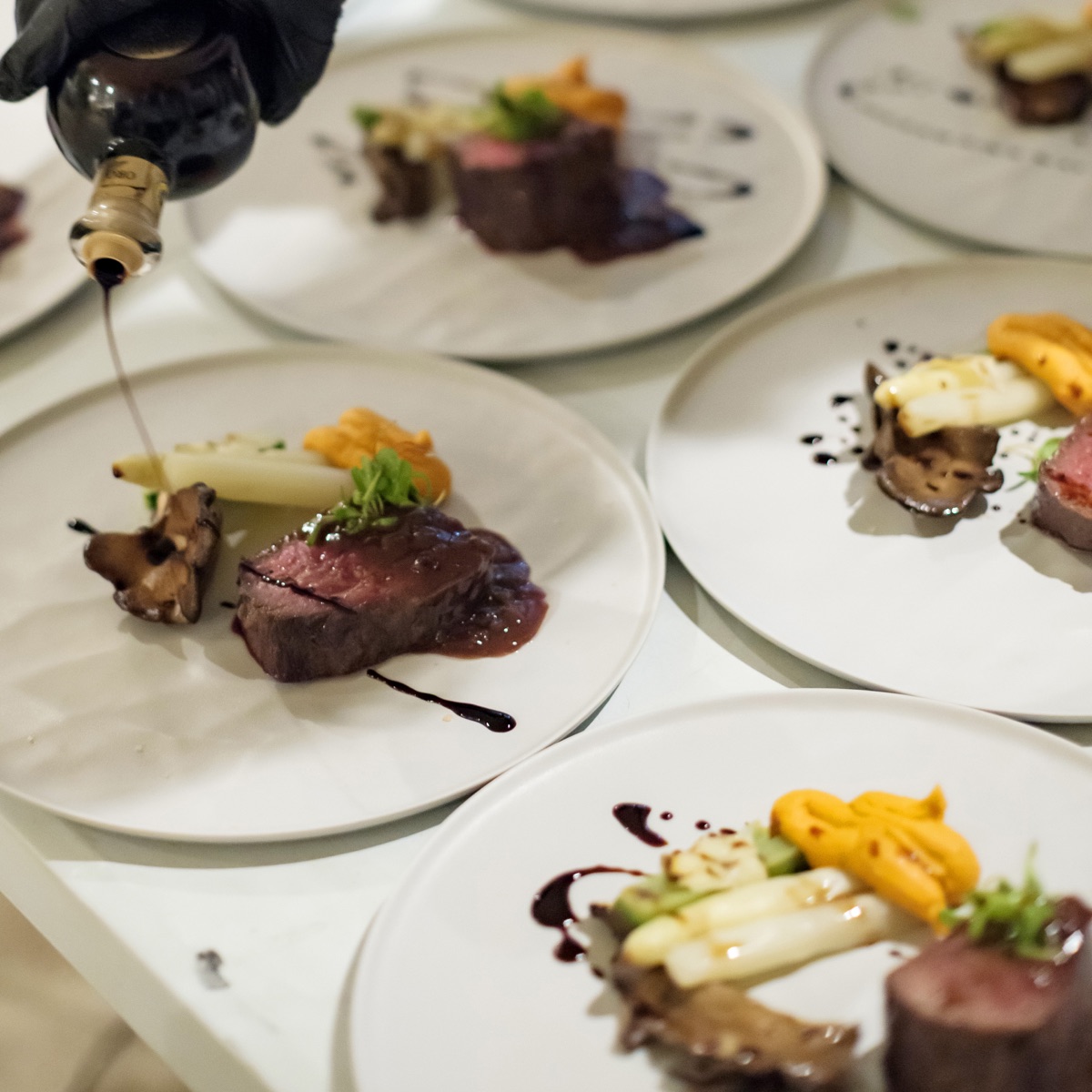 Plated meat dishes being finished with sauce before service