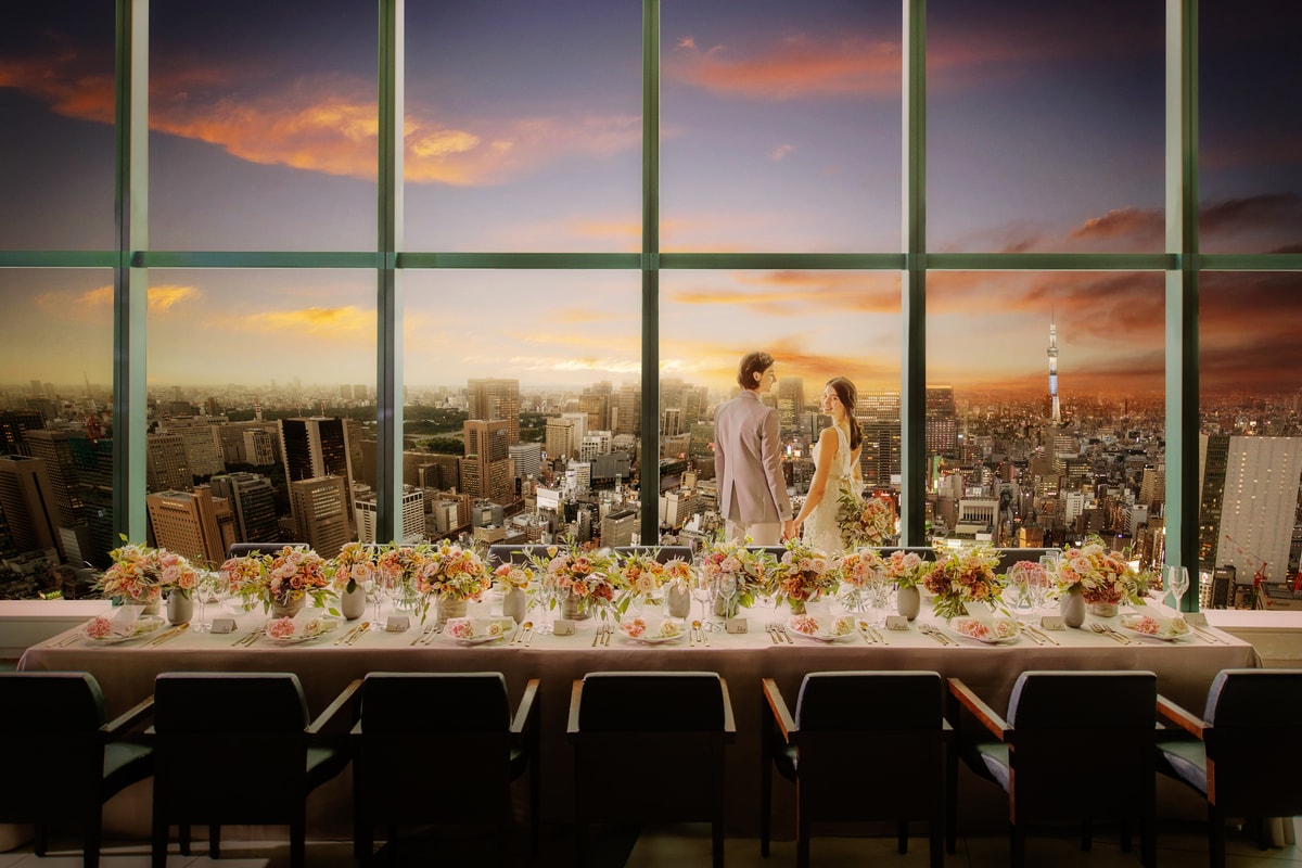 A couple beside a long reception table overlooking the sunset skyline