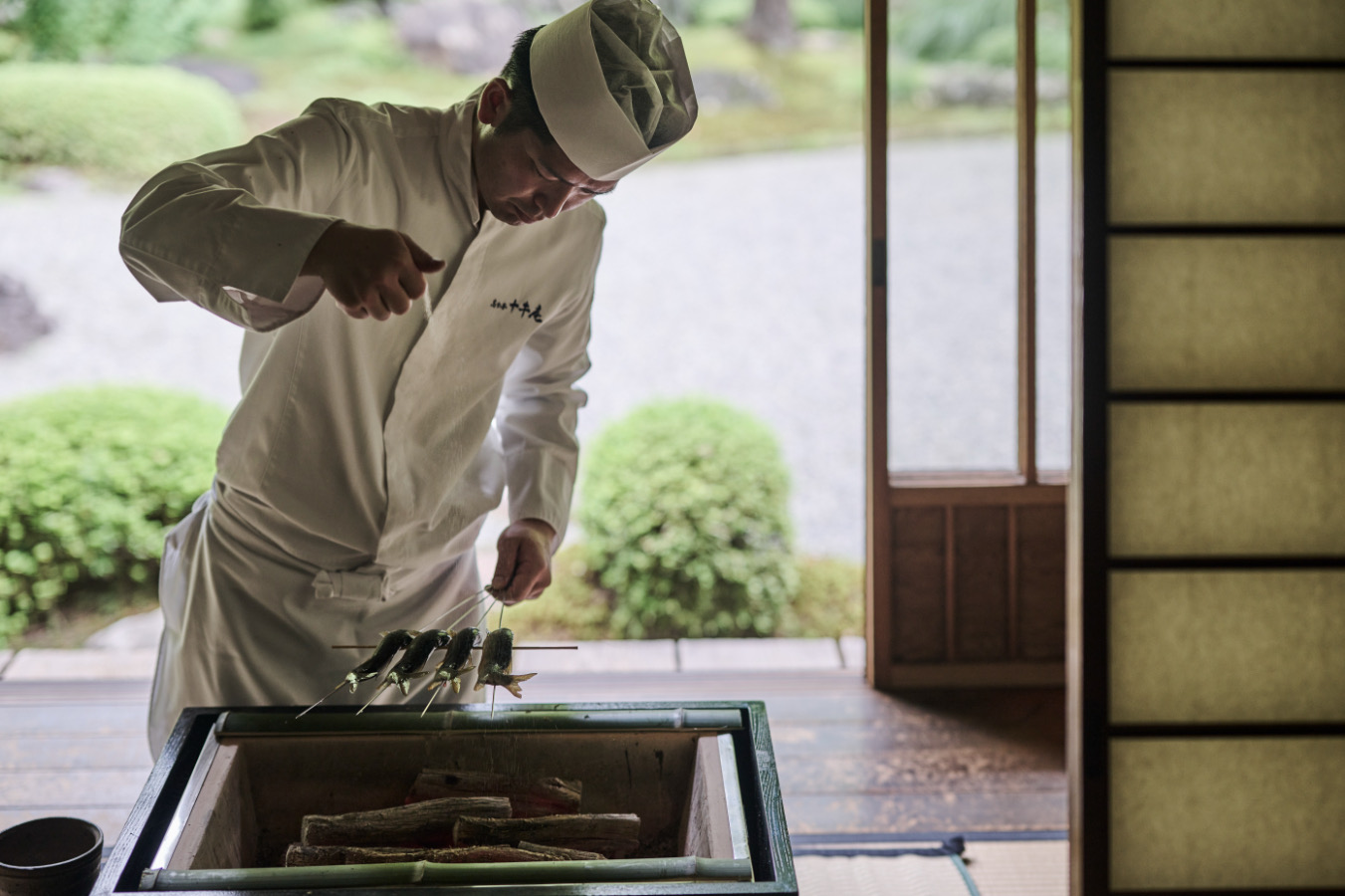 A chef grilling fish over a traditional hearth