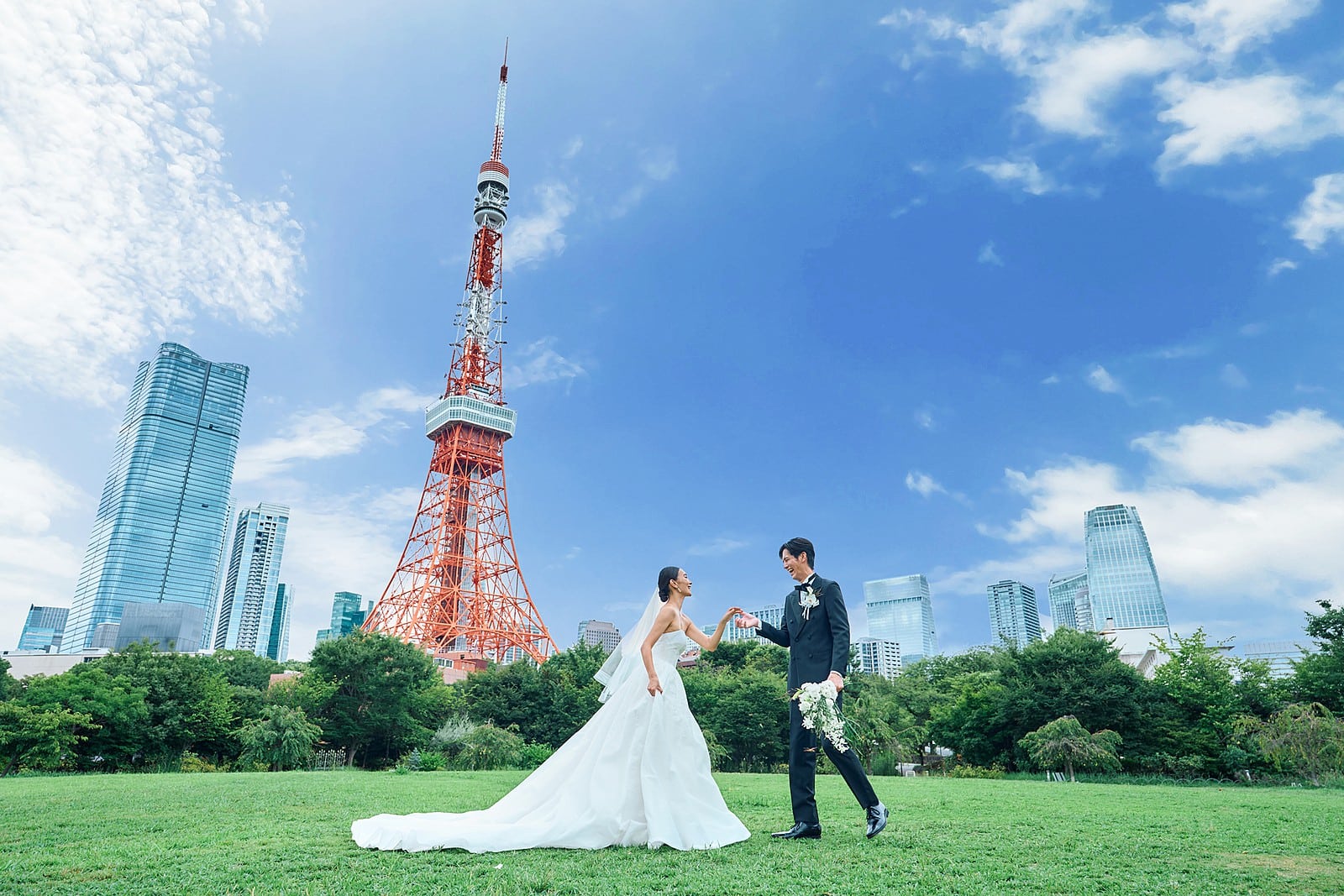 A wedding couple holding hands on a lawn in front of Tokyo Tower