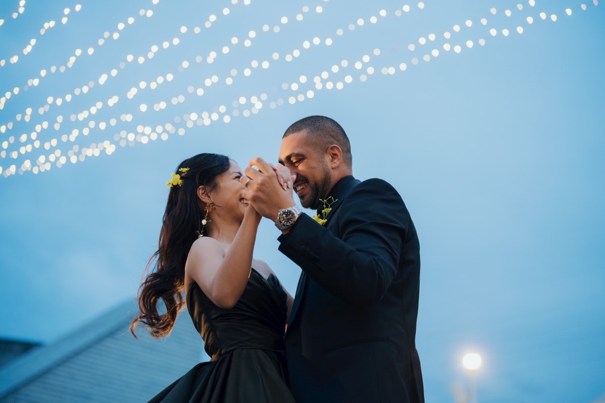 A wedding couple dancing beneath strings of lights at dusk