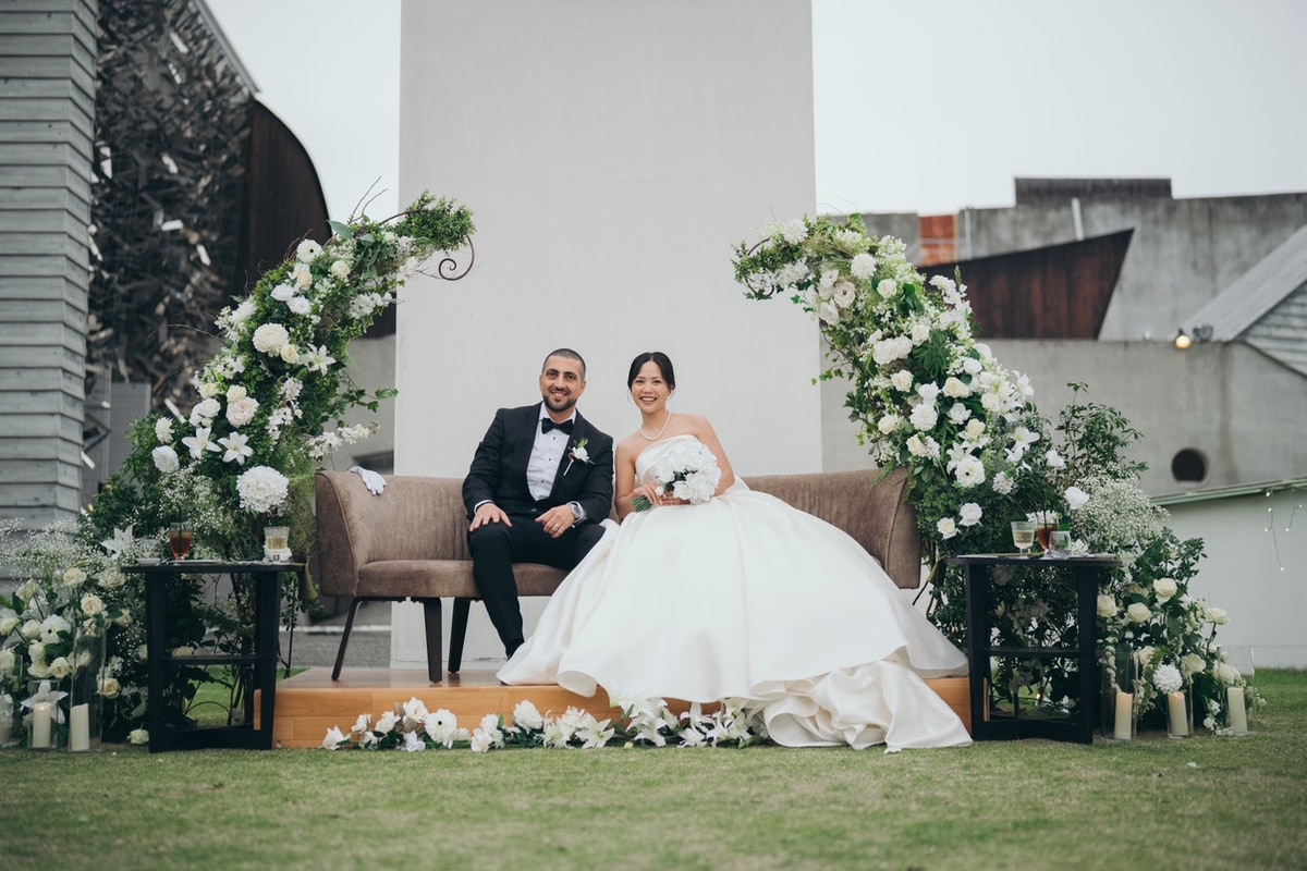 A wedding couple seated beneath white floral arches in the garden