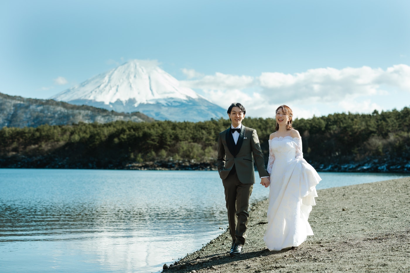 A wedding couple walking beside a lake with snow-covered Mount Fuji behind them