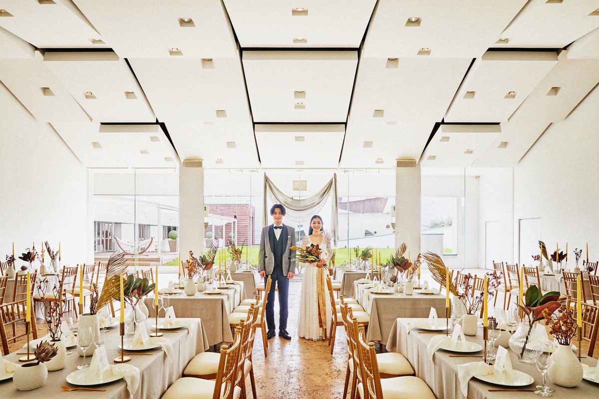 A wedding couple standing in a bright reception room with banquet tables